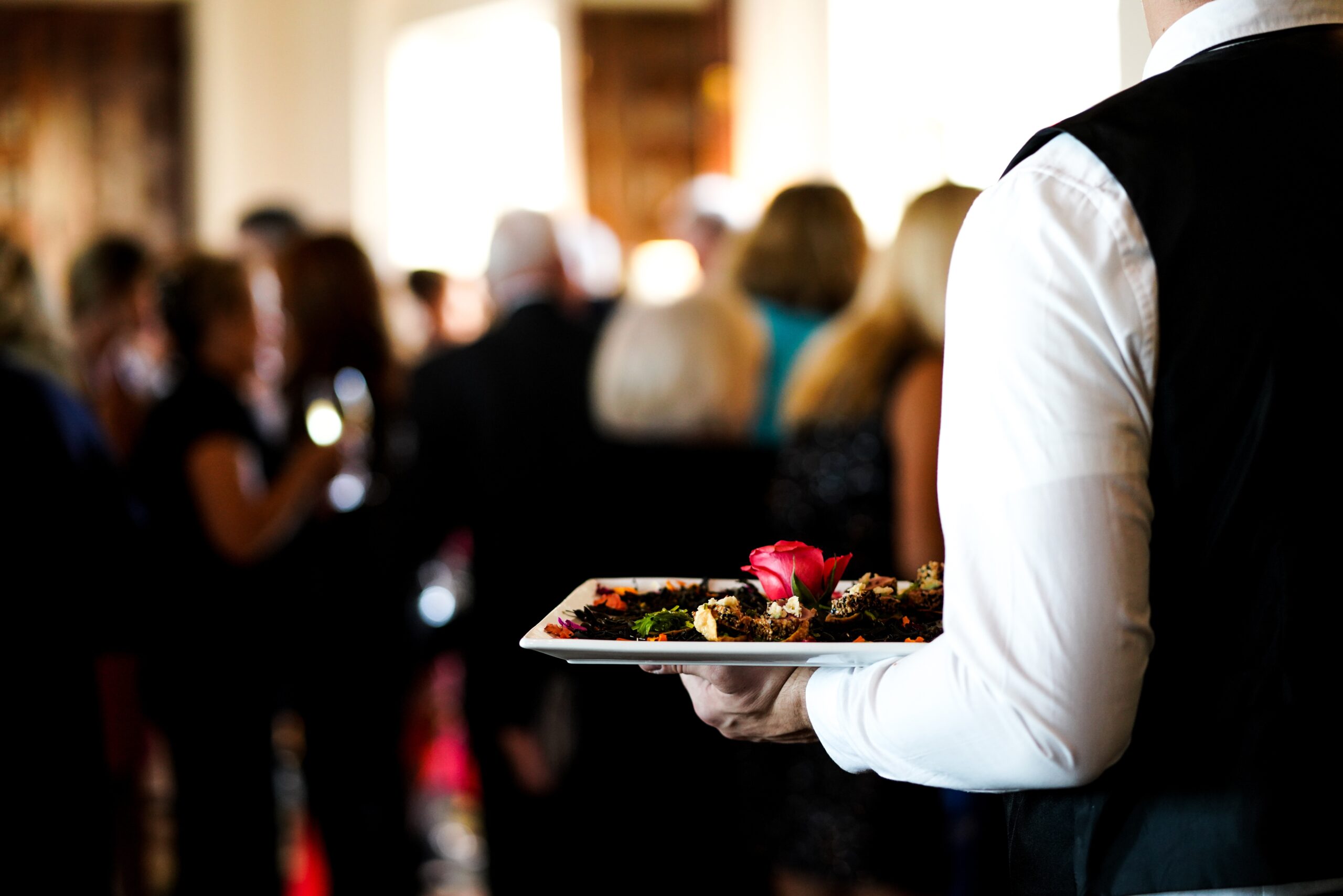 A closeup shot of a waiter's arm carrying a plate of a dish with a pink rose in it